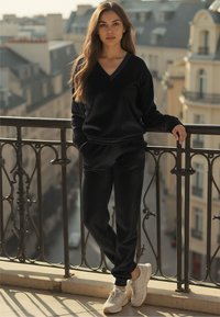 Zwarte, lange mouwen, V-hals sweatshirt gecombineerd met bijpassende joggers; zachte textuur. Witte sneakers met zilveren accenten maken de outfit compleet.