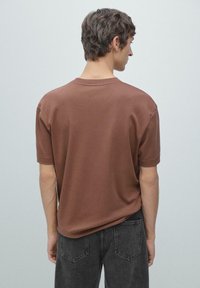 Bruin katoenen T-shirt met korte mouwen en een ronde halslijn. De stof heeft een gladde textuur, met een losse pasvorm en zonder zichtbare merknamen.