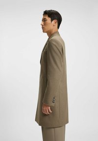 Lang, lysebrun frakke lavet af tekstureret stof. Har en notch-lapels, en enkelt brystlomme og manchetter med tre knapper. Skræddersyet pasform.