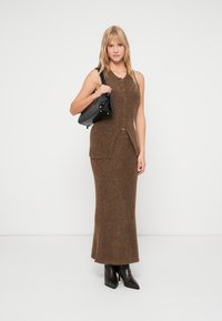 Robe sans manches en mélange de laine marron avec des boutons, une fente sur le devant et une silhouette ajustée ; associée à un sac à main noir et des bottines.