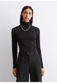 Schwarzes Rollkragenoberteil aus weichem Stoff, mit langen Ärmeln und figurbetontem Design, kombiniert mit schwarzen gestreiften Hosen. Silberne Halskette.