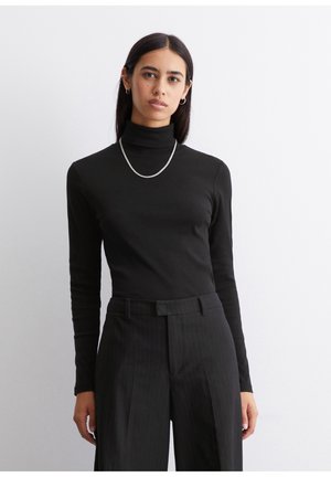 Zwarte coltrui van zachte stof, met lange mouwen en een aansluitend ontwerp, gecombineerd met zwarte pinstripe broeken. Zilveren ketting.