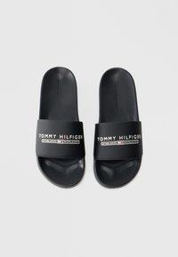 Fekete csúszó szandálok matt felülettel, széles pánton "TOMMY HILFIGER" logóval és alapítási dátummal, textúrált talpbetéttel, puha anyagból.