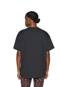 Μαύρο oversized μπλουζάκι με στρογγυλή λαιμόκοψη και κοντά μανίκια, κατασκευασμένο από μαλακό βαμβάκι. Η πίσω όψη δείχνει μια λεία υφή και άνετη εφαρμογή.