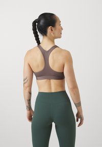 Soutien-gorge de sport marron avec un design dos nageur, associé à un legging vert taille haute. Tissu lisse avec des détails de coutures minimales.