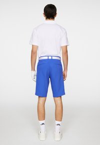 Niebieskie szorty golfowe o gładkiej fakturze, z przednimi kieszeniami i białym paskiem. Zestawione z prostą, białą koszulką polo i białymi skarpetkami z logo.