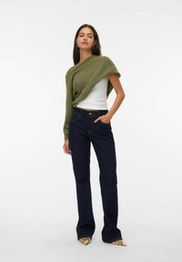 Groene gebreide sjaal over een witte top, gecombineerd met donkerblauwe flared jeans en puntige schoenen met een slangenprint.
