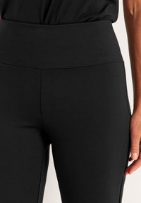 Schwarze Leggings aus einem glatten, dehnbaren Stoff. Hoher Bund und Nahtdetails an der Vorderseite. Enganliegendes Design.