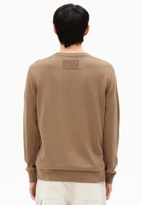 Brauner Pullover mit langen Ärmeln, rippenbündchen und einem kleinen strukturierten Aufnäher auf der Rückseite. Weiches Material und lockere Passform.