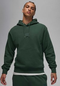 Ciemnozielona bluza z kapturem wykonana z miękkiego materiału. Posiada kieszeń z przodu i regulowane sznurki. Pod spodem szara koszulka.