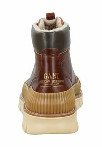 Brązowe skórzane botki za kostkę z beżową gumową podeszwą, teksturowanymi akcentami i miękką podszewką wewnętrzną. Posiadają wytłoczone logo z tyłu.