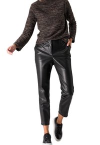 Zwarte nep leren broek met een hoge taille, taps toelopende pijpen en een gladde textuur, gecombineerd met een gestructureerde bruine top met lange mouwen en zwarte sneakers.