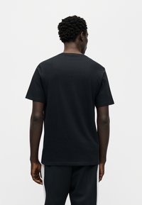 Μαύρο βαμβακερό μπλουζάκι με κλασική γραμμή, κοντά μανίκια και στρογγυλή λαιμόκοψη, εμφανιζόμενο από πίσω σε απλό φόντο.