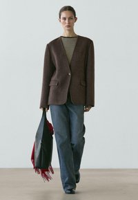 Brun uldblazer med en enkelt knap, kombineret med en stribet top og blå højtaljede jeans. En sort stor taske og et rødt tørklæde fuldender looket.