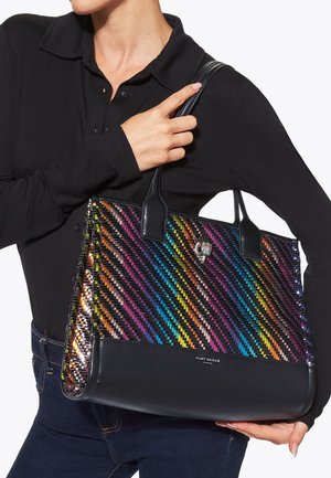Person wearing black long-sleeve shirt and jeans holding large handbag with multicolored woven pattern and black leather handles.