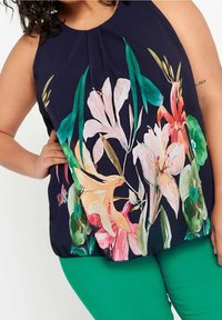 Ärmellös topp med blommönster på marinblå bakgrund, med rosa, orange och gröna blommor. Matcher med enfärgade gröna byxor. Slät textur.