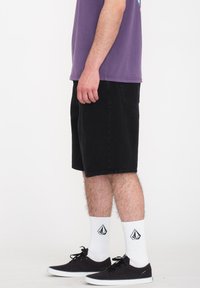 Shorts en jean noir avec une coupe décontractée, associés à un t-shirt violet, des baskets noires et des chaussettes blanches avec un logo.