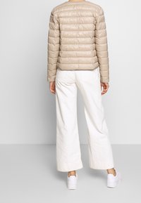 Giacca a puffo beige con cuciture orizzontali, design corto e maniche lunghe, abbinata a pantaloni bianchi a vita alta e larghi, e sneakers bianche.