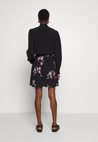 Blusa nera con maniche a sbuffo, abbinata a una gonna nera corta con motivi floreali rosa su uno sfondo a pois texturizzato.