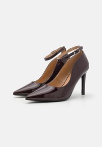 Burgunder patent lær høyhælte pumps med spisse tær, ankelstropper og et elegant design, som har en beige innside og en blank overflate.