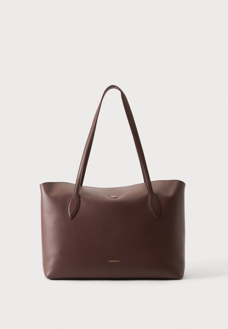 Sac cabas en cuir brun texturé avec de longues anses et un subtil logo de marque doré au centre avant, sur fond blanc uni.