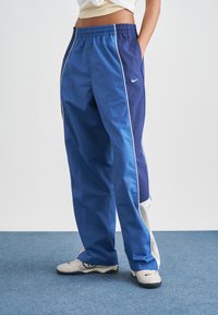 Μπλε αθλητικό παντελόνι με χαλαρή εφαρμογή, με αντιθετικές σκουρόχρωμες μπλε πλαϊνές πινακίδες, λευκές ρίγες και ελαστική ζώνη μέσης.