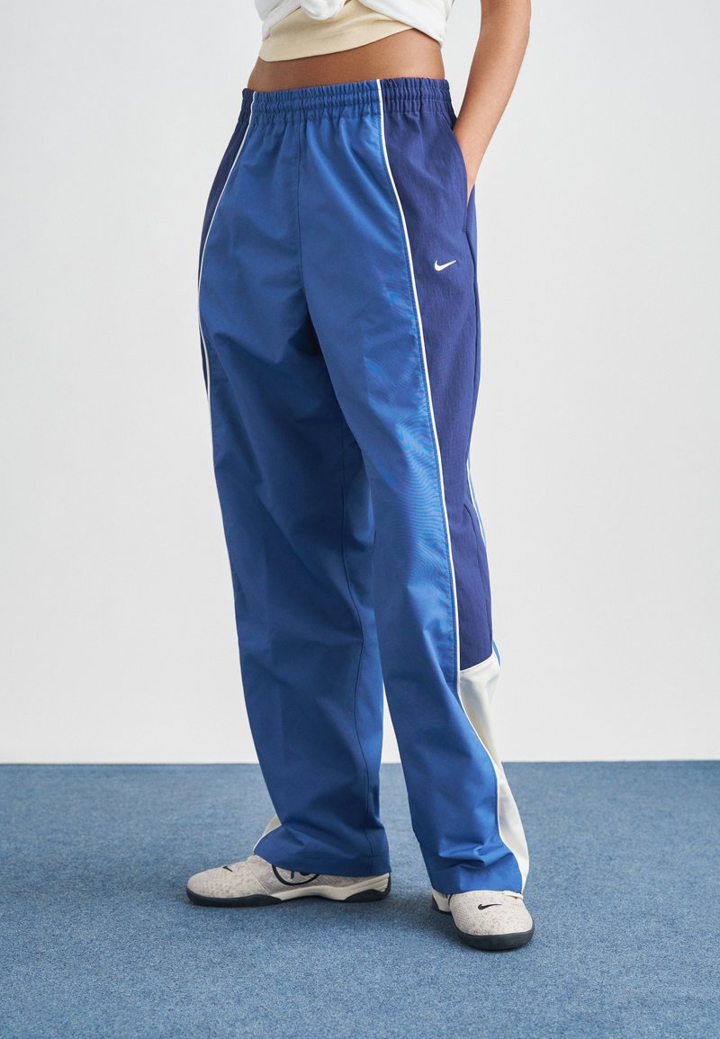 Μπλε αθλητικό παντελόνι με χαλαρή εφαρμογή, με αντιθετικές σκουρόχρωμες μπλε πλαϊνές πινακίδες, λευκές ρίγες και ελαστική ζώνη μέσης.