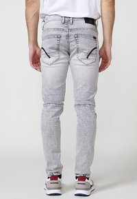 Grå strækdenim jeans med en slidt overflade, der har to baglommer med lynlåse og et slim fit design.