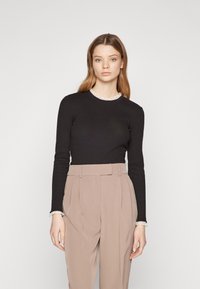 Svart langermet topp med en volanghvit krage, sammen med beige høyt liv bukser med legg og en skreddersydd passform.