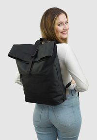 Zwarte rugzak met een oprolontwerp, gemaakt van gladde stof, met een voorkant ritsvak en verstelbare schouderbanden. Eenvoudig en functioneel ontwerp.
