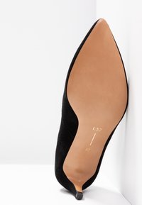 Chaussure noire à bout pointu avec un petit talon, montrant une semelle lisse couleur tan marquée de la pointure 37 et du code de la marque L37.