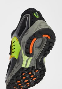 Černá a šedá sportovní bota s texturovanou podrážkou a jasně oranžovými a neonově zelenými akcenty, síťovanými panely a robustním designem.
