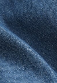 Tissu en denim d'une couleur bleu profond, présentant une texture lisse avec un léger éclat et de subtiles variations dans le motif de tissage.