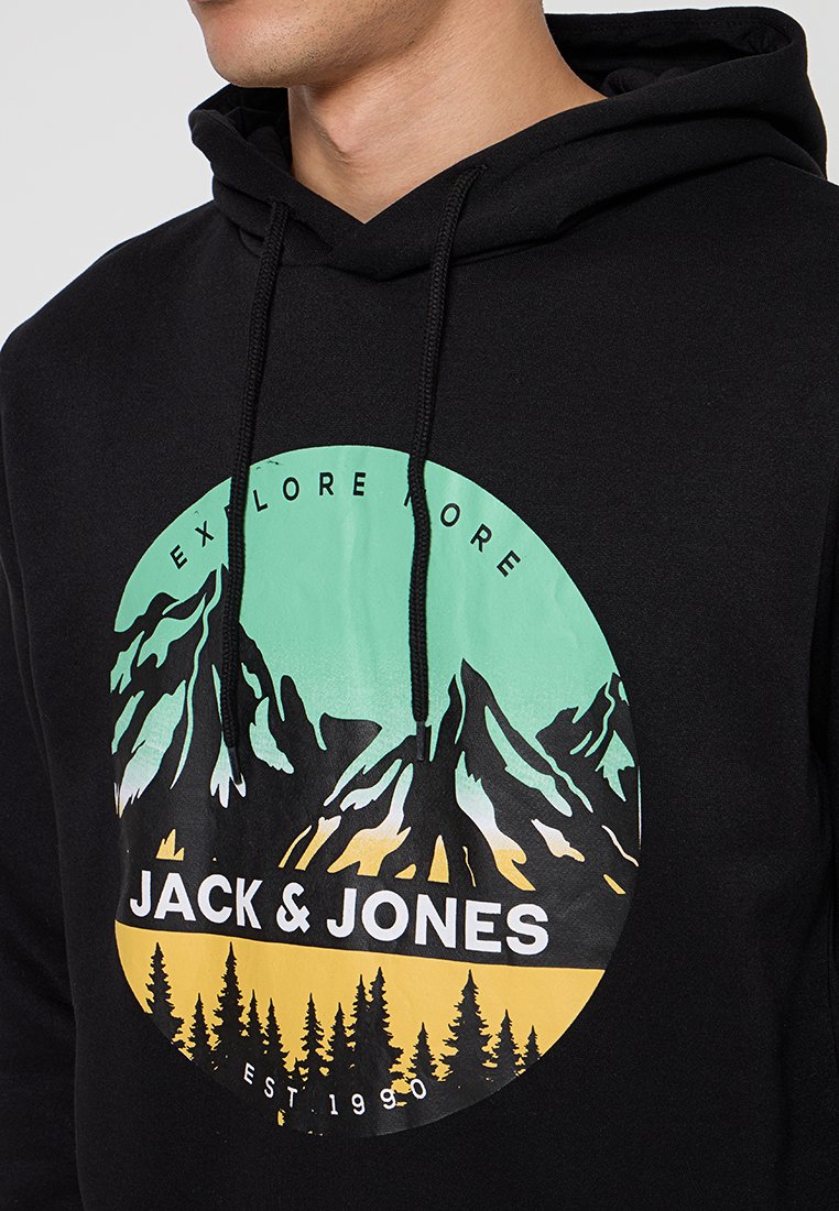 Zwarte hoodie met een groot cirkelvormig graphic van groene bergen, gele zonsondergang en de tekst "JACK & JONES" in het wit. Koordjes zijn inbegrepen.