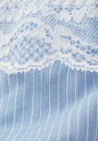 Lichtblauwe stof met fijne witte strepen en ingewikkelde witte kantafwerking langs de bovenrand. Zachte textuur met delicate details.