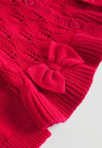 Roter gestrickter Cardigan mit strukturiertem Design, gerippten Bündchen, Knopfverschluss und einem auffälligen Schleifenakzent auf der Vorderseite.