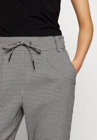 Svartvitt hounds-tooth mönstrade byxor med elastisk midja och dragsko, med en framficka och en slät, vävd textur.
