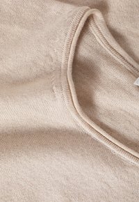 Pull en tricot beige avec un col rond. Texture douce, finition lisse et détails de couture visibles le long du col et de l'ourlet.