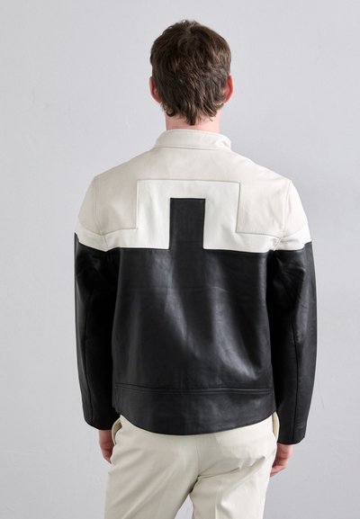 Black and cream leather jacket with a structured design, featuring a prominent cross detail on the upper back and smooth texture.