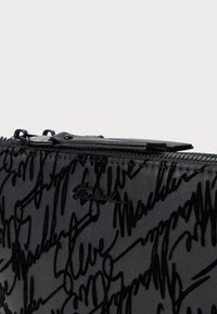 Borsa a zip nera realizzata in materiale sintetico testurizzato con motivo in rilievo della firma. La minuteria nera completa il design.