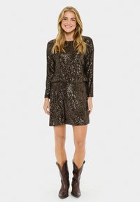 Vestido de lentejuelas marrón oscuro con mangas largas, cintura ajustada y falda acampanada. Combinado con botas de vaquero marrones, de superficie texturizada y brillante.