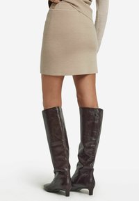 Beige gebreide minirok met een aansluitend ontwerp, gecombineerd met glanzende kniehoge bruine leren laarzen met een lichte hak.