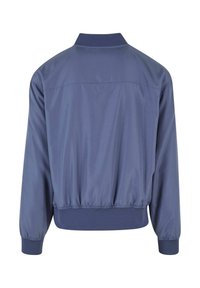 Veste légère bleue à manches longues, poignets et taille élastiques, vue de dos sur fond blanc.