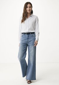 Ljust blå vida jeans med hög midja, ihop med en vit skjorta med knappar och ett svart bälte med vita prickar. Svarta öppna klackar.