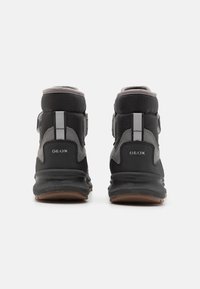 Zapatillas altas negras con acentos grises, que cuentan con un cuello acolchado, refuerzo en el talón y una suela de goma. Logo de Geox visible en los laterales.