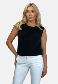 Czarny bezrękawnik z fałdowanym dekoltem, w zestawieniu z białymi dopasowanymi spodniami. Gładki materiał o delikatnym połysku, oferujący czysty, elegancki wygląd.