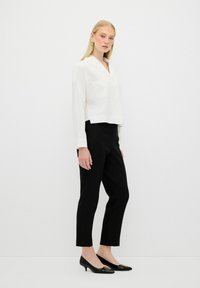 White, cropped button-up shirt with a chest pocket, paired with black, tailored, ankle-length pants. Model wearing black heels with gold accents.