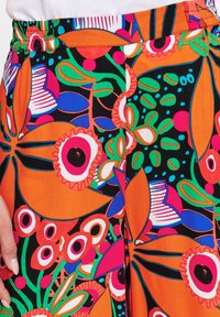 Bunte Blumenhose in lebhaftem Orange, mit großen pinken, grünen und schwarzen Mustern sowie kreisförmigen Akzenten und einem lässigen Schnitt.