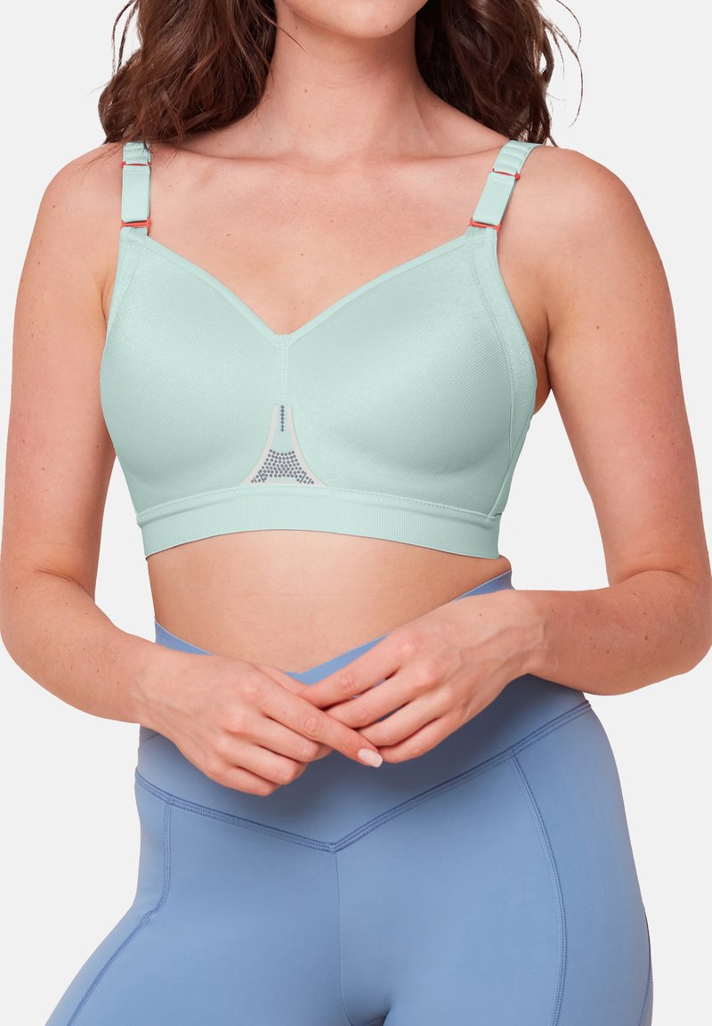 Lys myntegrønn sport-bh med sømløst design, justerbare stropper og mesh-detalj i midten. Kombinert med høyhalsede blå leggings.