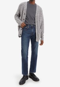 Light gray wool cardigan with large buttons over a dark gray crew-neck shirt. Worn with dark blue straight-leg jeans and black lace-up shoes.